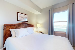 A neatly made bed with a wooden headboard, a bedside lamp, and a framed picture on the wall. - Oceanfront condo with scenic balcony & washer/dryer - pool/hot tub/tennis access (Panama City Beach)