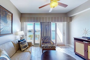 Ein Wohnzimmer mit einer Couch, einem Sessel und einem Holztisch. Es gibt einen Deckenventilator, eine Lampe und ein Schrank.