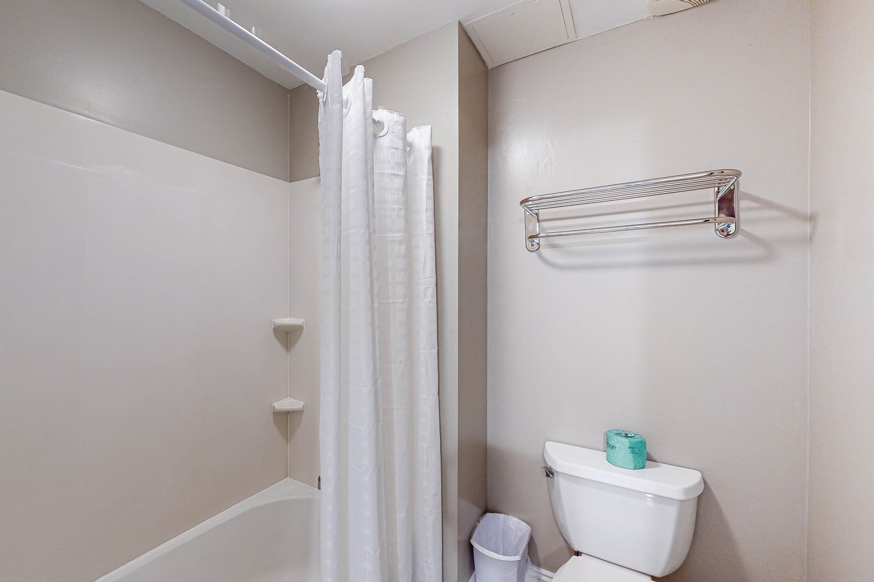 A bathroom with a bathtub, a shower curtain, a toilet, and a metal shelf.