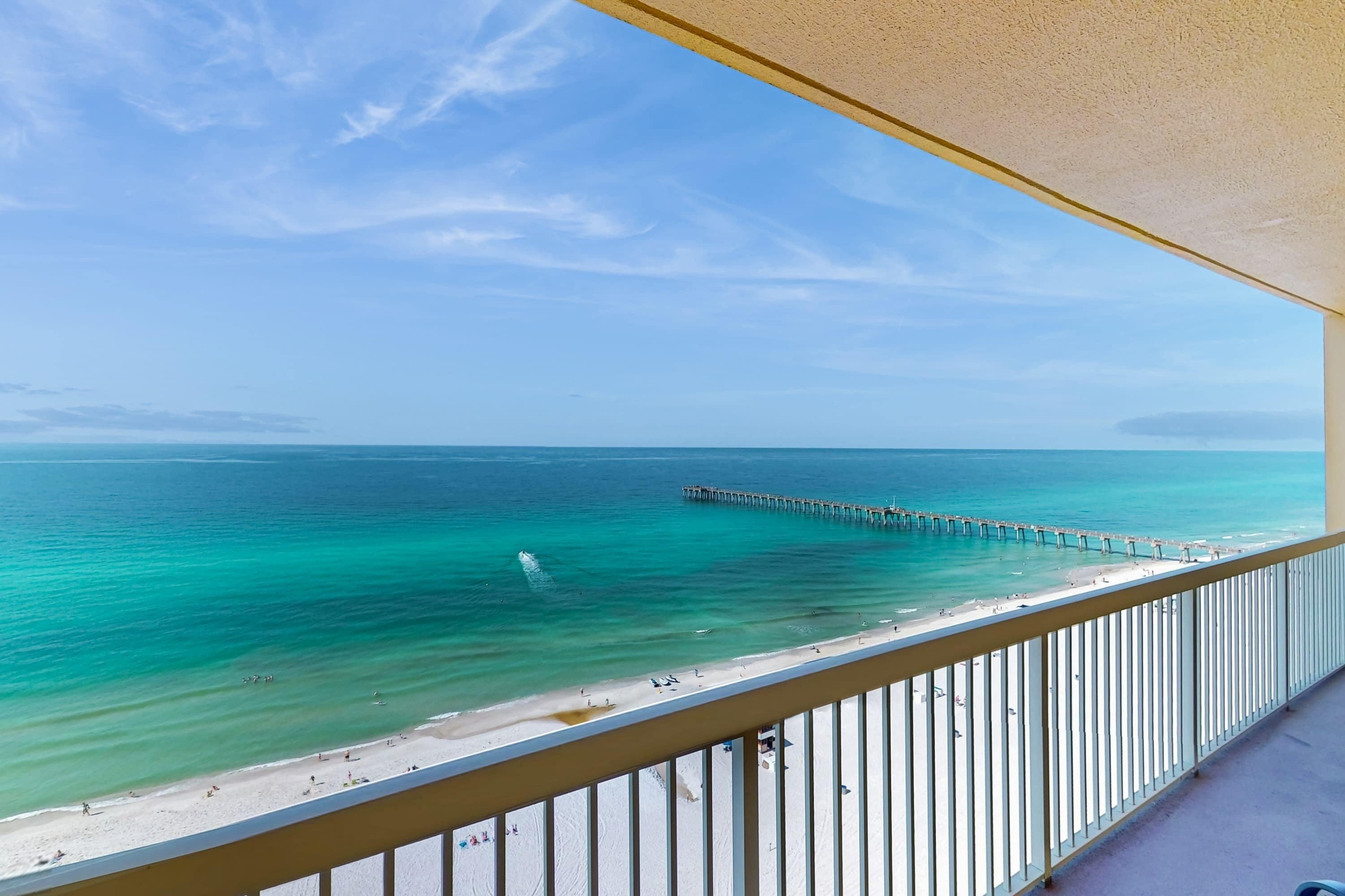 A balcony with a view of a beach and a pier extending into the ocean.