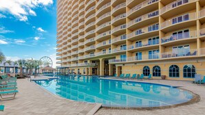 A hotel with a large pool, multiple balconies, and a Ferris wheel in the background. - Ocean-view 10th-floor condo with balcony, heated outdoor pool, hot tub, gym, W&D (Panama City Beach)
