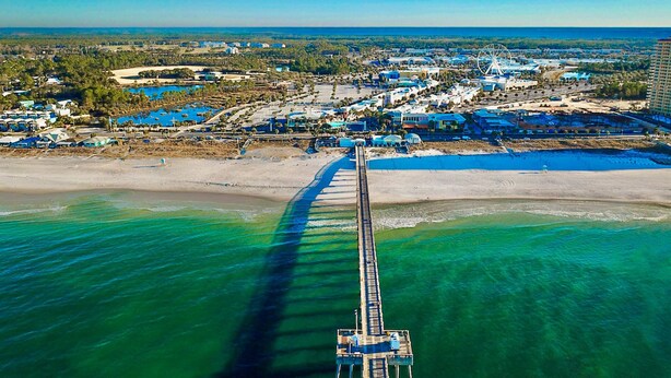 An aerial view of a coastal area with a long pier extending into the water, surrounded by buildings and a beach. - Ocean-view 10th-floor condo with balcony, heated outdoor pool, hot tub, gym, W&D (Panama City Beach)