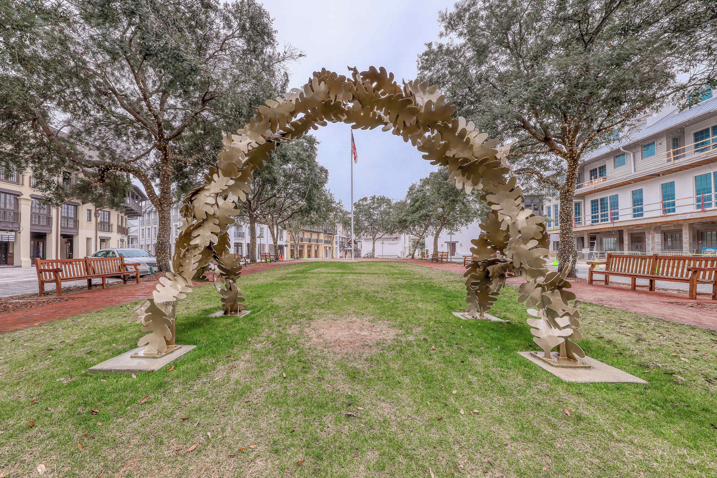 An outdoor sculpture installation in a park with benches and buildings in the background.