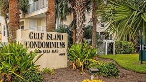 En skylt för Gulf Island Condominiums, med utsikt över den omgivande grönskan och en byggnad i bakgrunden.