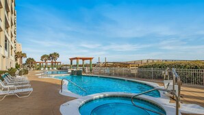 A pool area with lounge chairs, a hot tub, and a wooden deck. - 3rd-Floor Gulf-Front Condo w/Balcony, Shared Hot Tub, Heated Pool, & Fast WiFi (Navarre Beach)