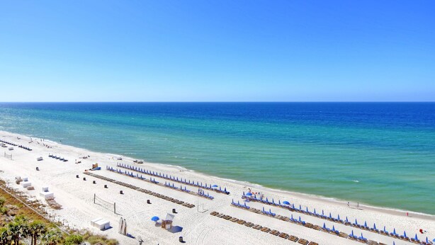 Una playa con arena blanca, sombrillas azules y un cielo azul despejado.