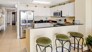 Cocina moderna con armarios blancos, encimera negra y tres taburetes verdes.