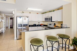 A modern kitchen with white cabinets, a black countertop, and three green bar stools. - Waterfront condo with balcony, pools, gym & central AC (Panama City Beach)