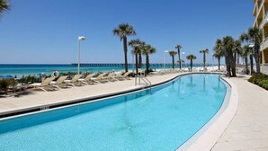 Una piscina con sillones de descanso y palmeras, un muelle al fondo y un cielo azul despejado.