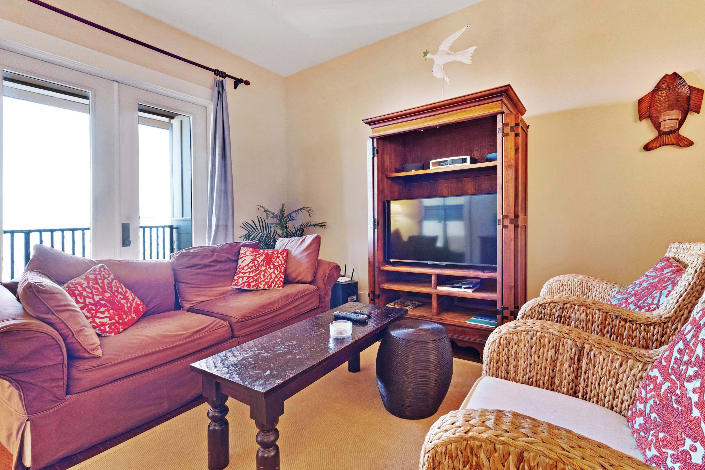 Una sala de estar con un sofá de cuero marrón, una mesa de centro de madera, un sillón de mimbre y un mueble para televisión.