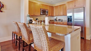A modern kitchen with wooden cabinets, a stainless steel refrigerator, a microwave, and a granite countertop. - Stunning condo with washer/dryer, pool & convenient beach access (Santa Rosa Beach)
