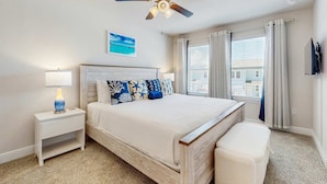 Quarto com cama, mesa de cabeceira, ventilador de teto, janela com cortinas e um quadro na parede.