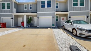 Uma fileira de casas geminadas de dois andares com garagens anexas, um caminho de acesso de concreto e um carro branco estacionado no caminho.