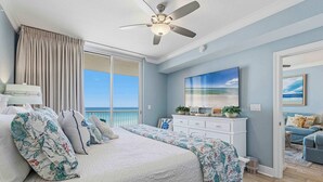 A bedroom with a bed, a ceiling fan, a dresser, a painting, and a view of the ocean. - Enchanting oceanfront condo with pool, balcony, fitness area, & washer&dryer (Fort Walton Beach)