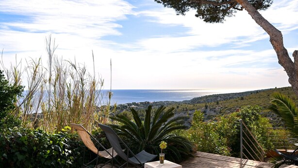 Eine Terrasse mit Stühlen und einem Tisch, mit Blick auf eine Küstenlandschaft.