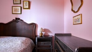 Ein Schlafzimmer mit einem Bett, einem Nachttisch mit Lampe, einer Kommode und drei gerahmten Bildern an der Wand.