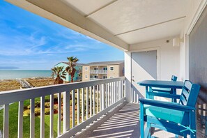 Un balcon avec vue sur la plage et l’océan, une balustrade blanche et des meubles bleus.