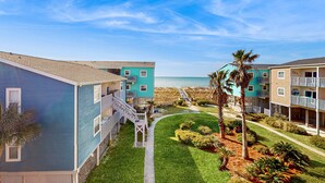 Un hôtel situé en bord de mer, composé de bâtiments à plusieurs étages, doté d’une allée centrale et d’un aménagement paysager bien entretenu.