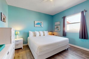 Une chambre à coucher avec un grand lit, une table de chevet avec une lampe, une commode et des œuvres d’art accrochées aux murs.