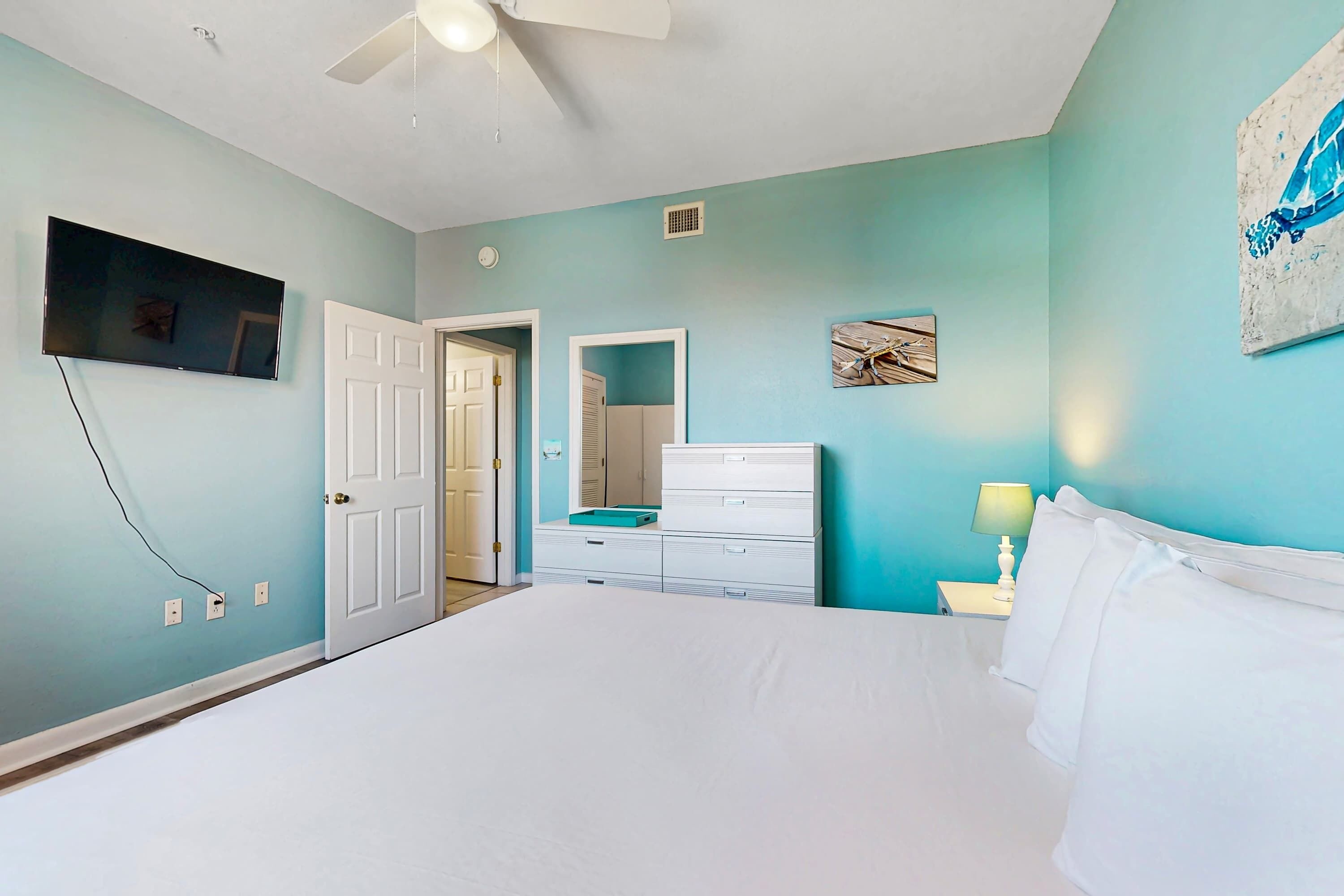 Une chambre à coucher comprenant un lit, une commode, un téléviseur et un ventilateur de plafond.