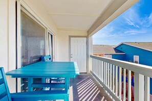 Un balcon avec une table et des chaises bleues, une porte blanche et une vue sur un immeuble bleu.