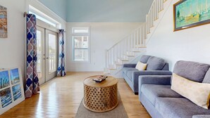A spacious living room with a grey sofa, a round wooden coffee table, and a staircase leading to an upper floor. - Spacious home with  shared pool, large kitchen and close to beach (Pensacola Beach)