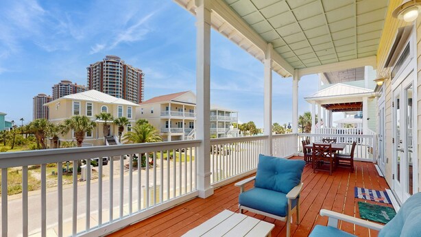 A wooden deck with white railings, blue outdoor furniture, and a covered area with a table and chairs. - Spacious home with  shared pool, large kitchen and close to beach (Pensacola Beach)