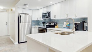 Una cocina moderna con armarios blancos, electrodomésticos de acero inoxidable, microondas y un lavabo con grifo moderno.