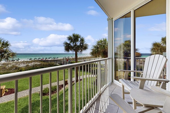A balcony with a view of the beach, a chair, and a table. - Gorgeous beachfront condo, shared pool and beach access (Fort Walton Beach)