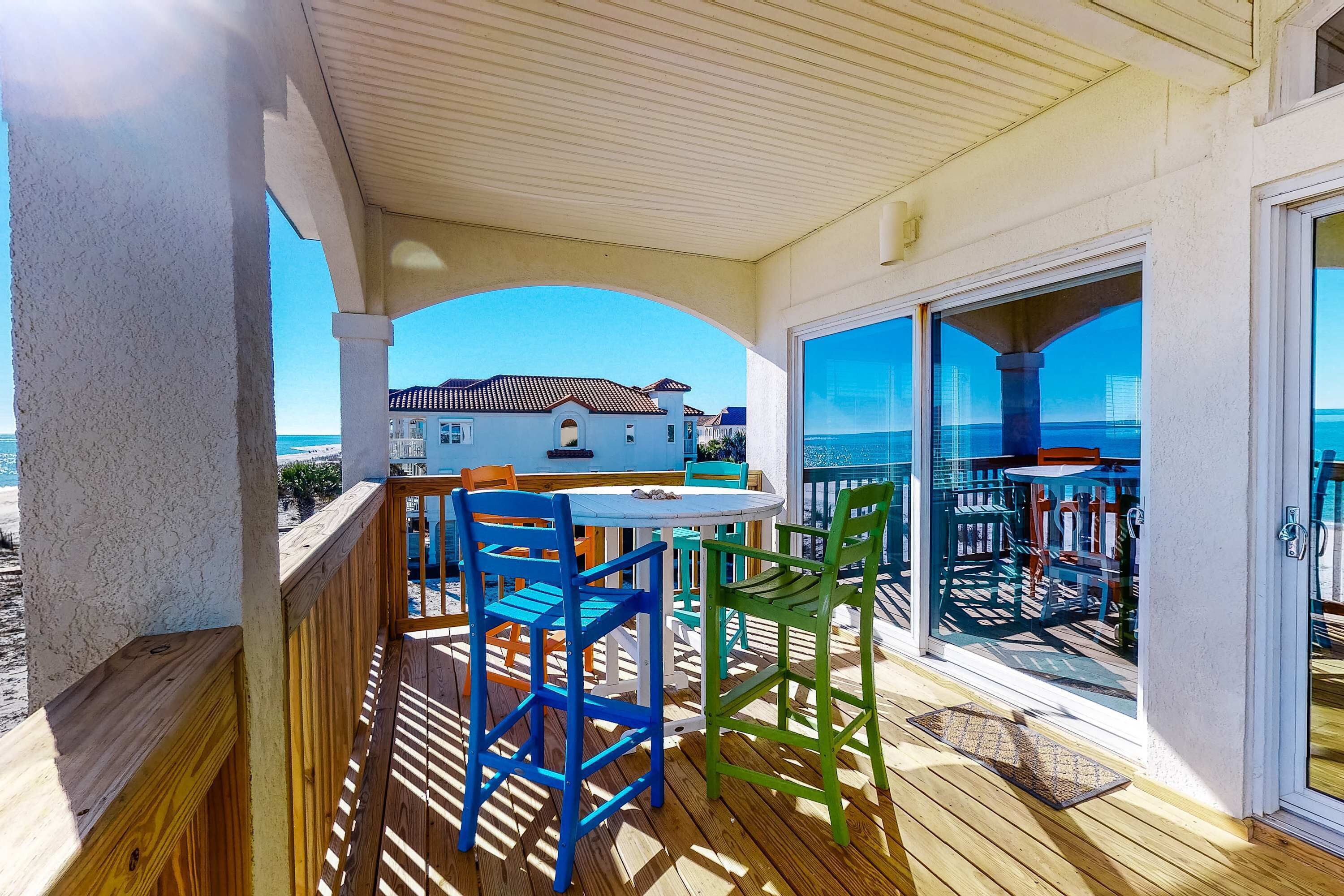 A covered outdoor area with a wooden deck, a round table, and colorful chairs.
