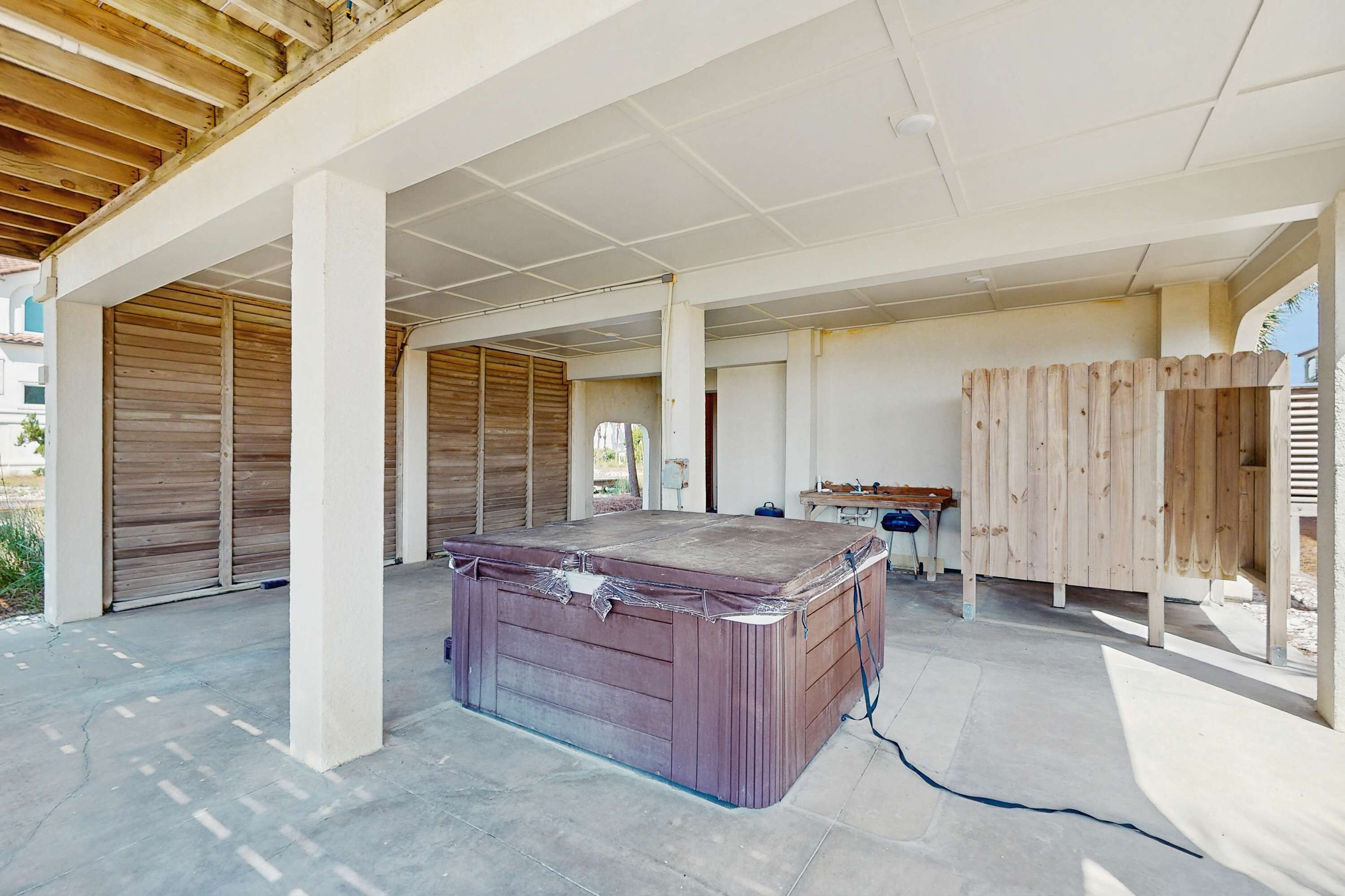 An outdoor covered area with a hot tub, wooden benches, and a table.