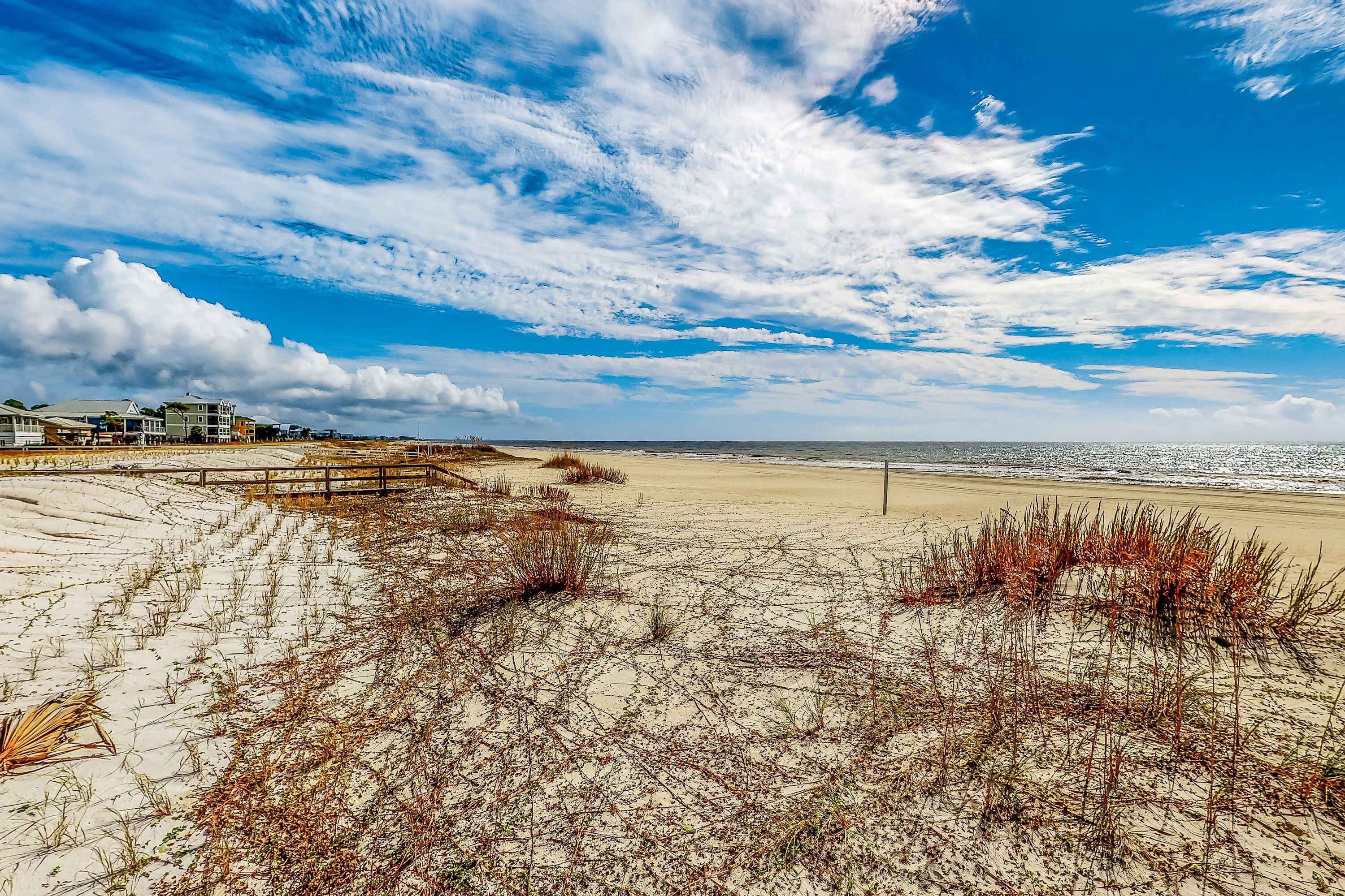 A beach with sand dunes, a wooden fence, and a building in the background.