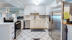 A modern kitchen with white cabinets, stainless steel appliances, and a tiled floor.