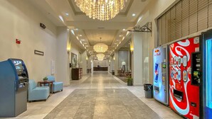 Un vestíbulo de hotel con candelabro, máquinas expendedoras y zonas de estar.