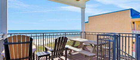 A wooden deck with Adirondack chairs and picnic tables overlooking a beach.