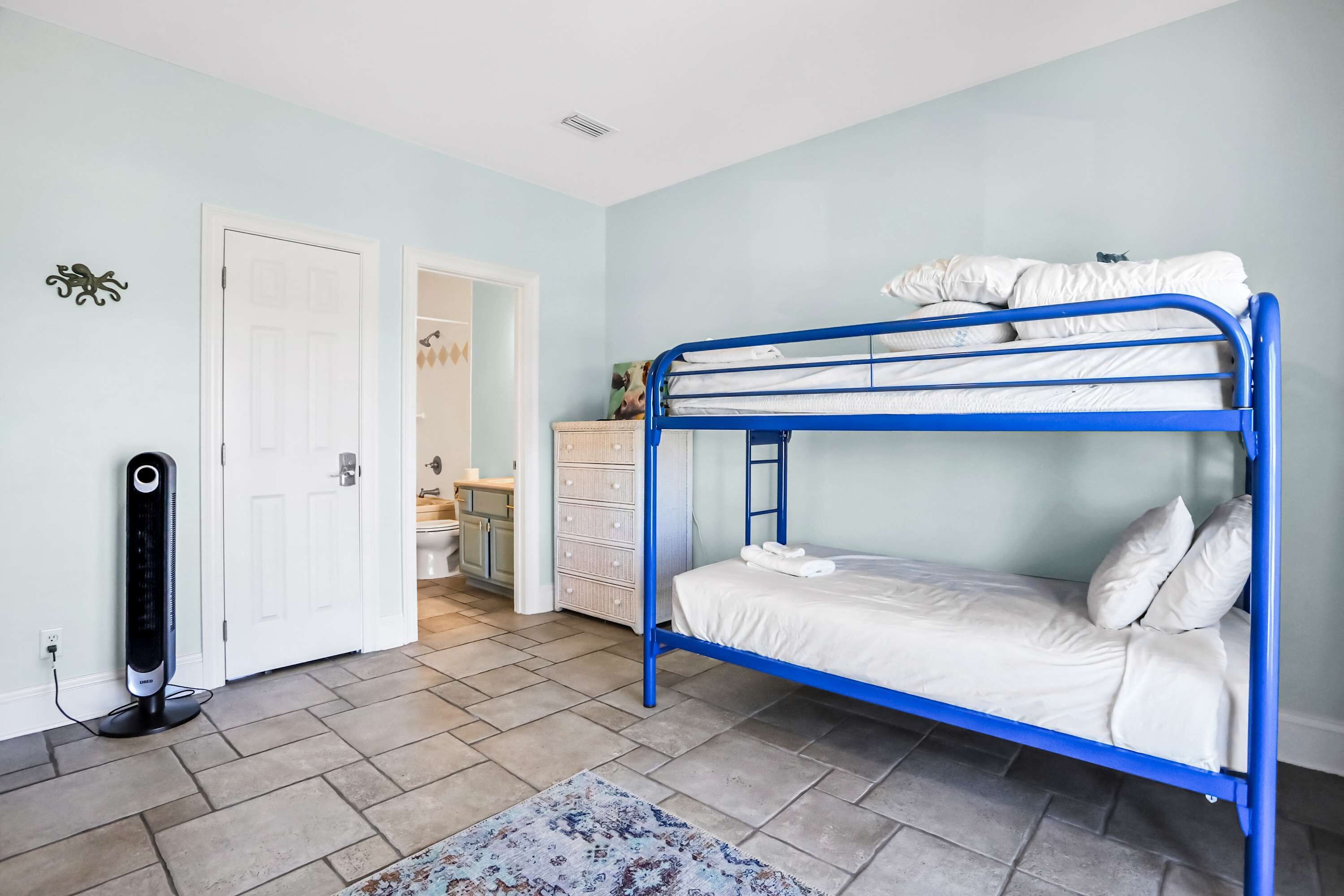 A room with a bunk bed, a standing heater, a door, and a small cabinet.