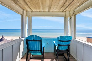 A covered balcony with two blue Adirondack chairs and a small table, overlooking a beach. - Beachfront home with pool, elevator, dog-friendly (St. George Island)