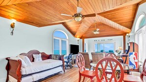 Quarto espaçoso com teto de madeira, uma cama, mesa de jantar com cadeiras e uma televisão.