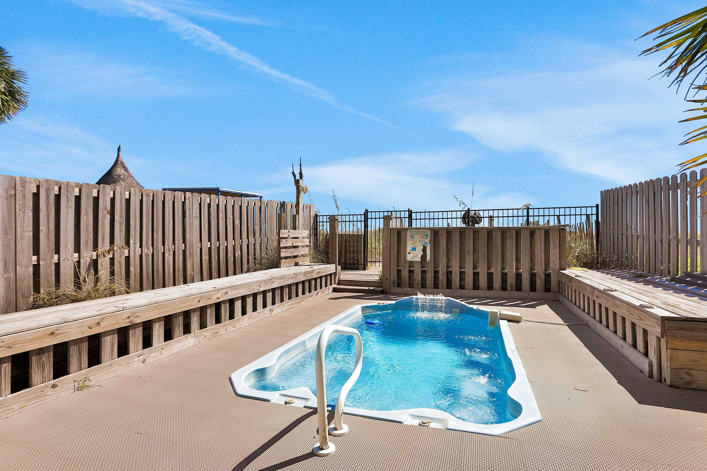 Una piscina rettangolare con un prendisole in legno che la circonda, racchiusa da una recinzione in legno.