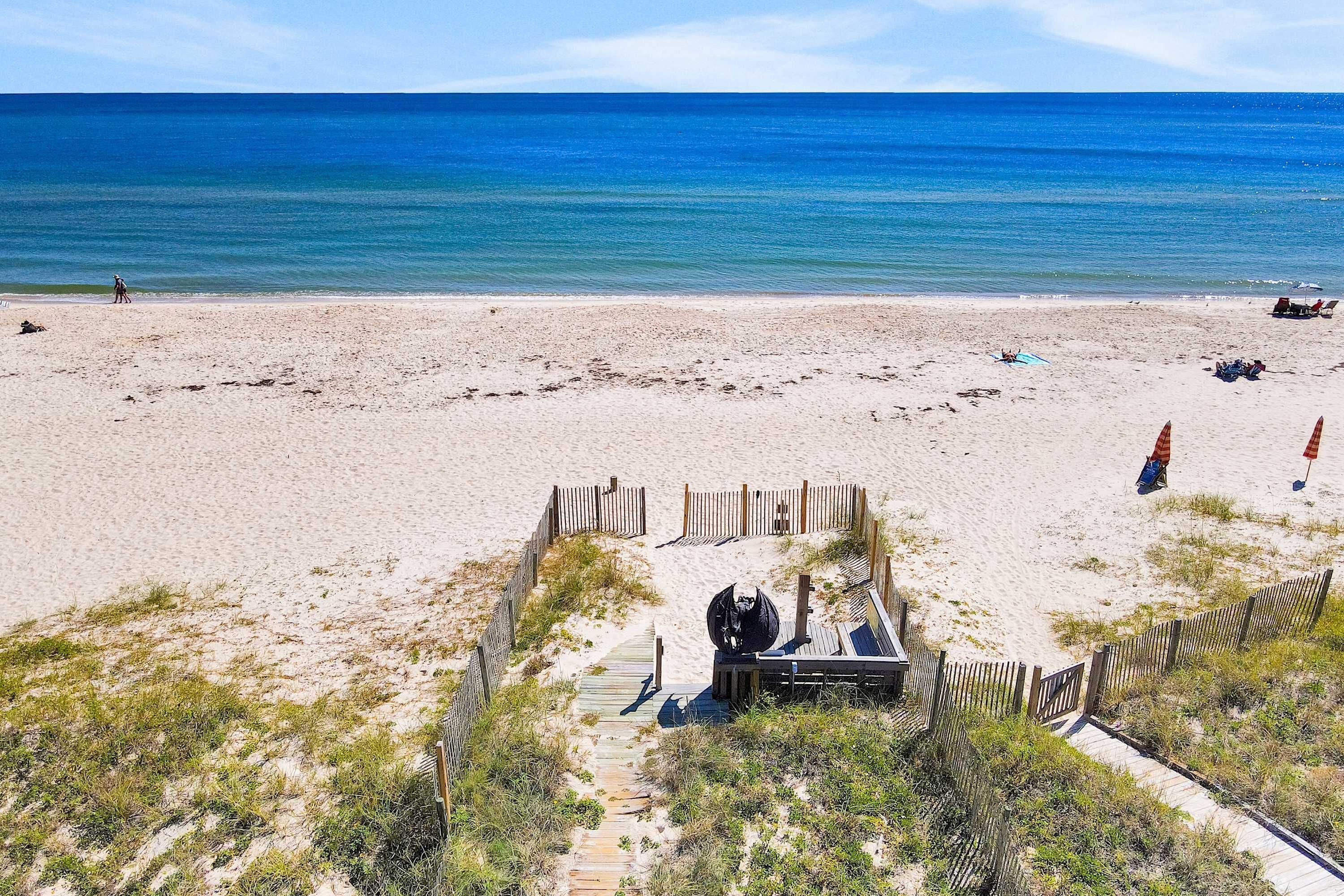Een strand met een houten looppad dat leidt naar een overdekt gebied met zitplaatsen.