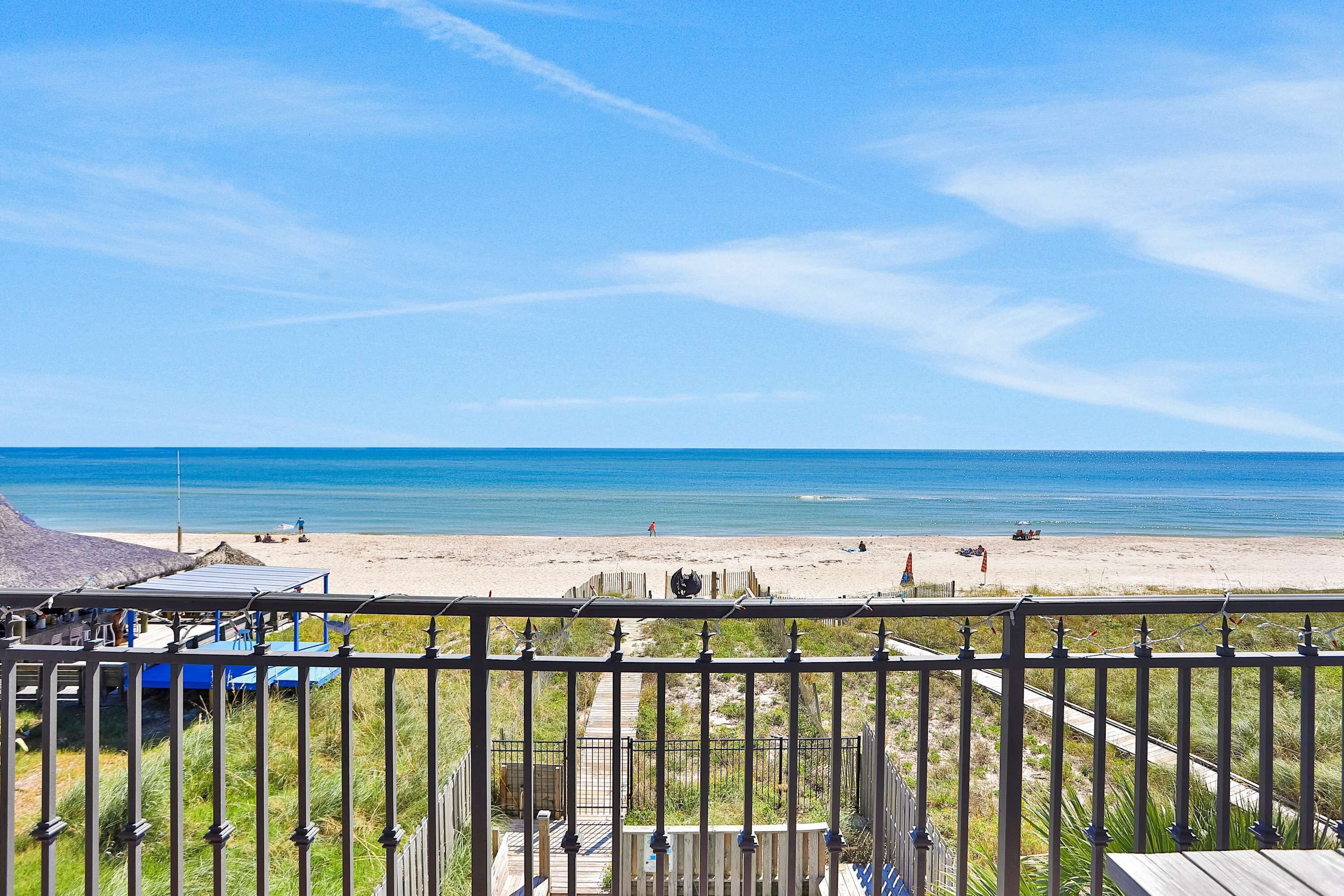 Blick auf einen Strand vom Balkon mit Holzdeck und Metallgeländer.