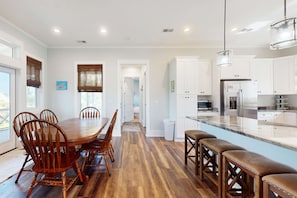 A modern kitchen with white cabinets, a large island, and a dining area with wooden chairs.