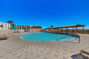 Una piscina con sillas de descanso y sombrillas, rodeada de edificios y un cielo azul despejado.