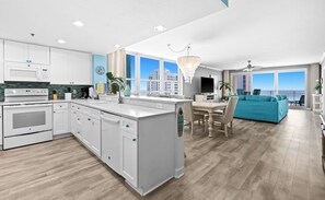 A modern kitchen with white cabinets, a central island, and a dining area with a blue sofa. - Stylish beach condo with gulf views, shared pool, gym & WiFi - walk to the beach (Destin)