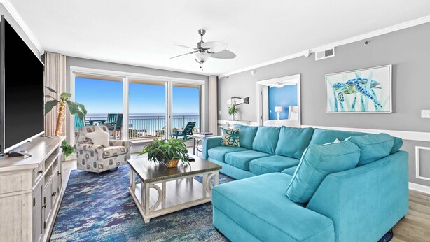 A living room with a teal sofa, a coffee table, and a TV. There is a balcony with a view of the ocean. - Stylish beach condo with gulf views, shared pool, gym & WiFi - walk to the beach (Destin)