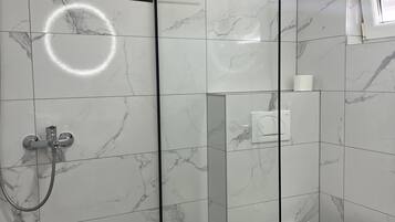 A modern bathroom with a glass shower enclosure, a toilet, and a small trash bin.