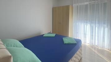 A bedroom with a bed, a wardrobe, and a window with sheer curtains.