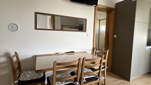 A dining area with a wooden table and chairs, a flat-screen TV mounted on the wall, a mirror above the table, and a refrigerator in the background. - Apartment Lavaran 4 in Vir (Vir)
