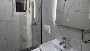 Un baño moderno con cabina de ducha de vidrio, inodoro y lavamanos con espejo.