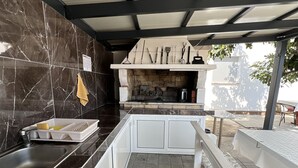 A modern outdoor kitchen with a stone backsplash, a built-in grill, and a dining area with a bench. - Apartment Lavaran 6 in Vir (Vir)